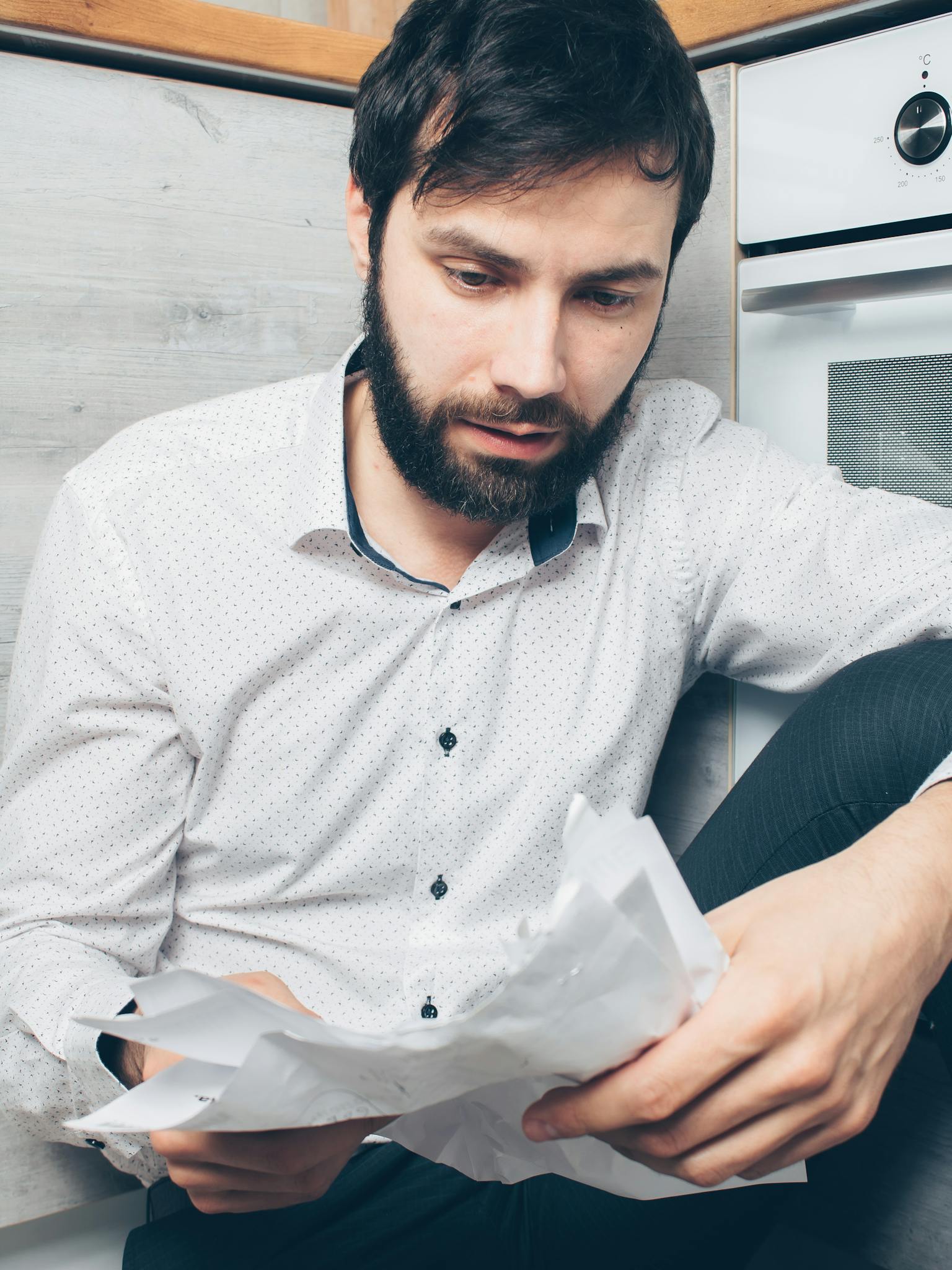 A worried man sitting indoors examining financial papers, depicting stress and concern.